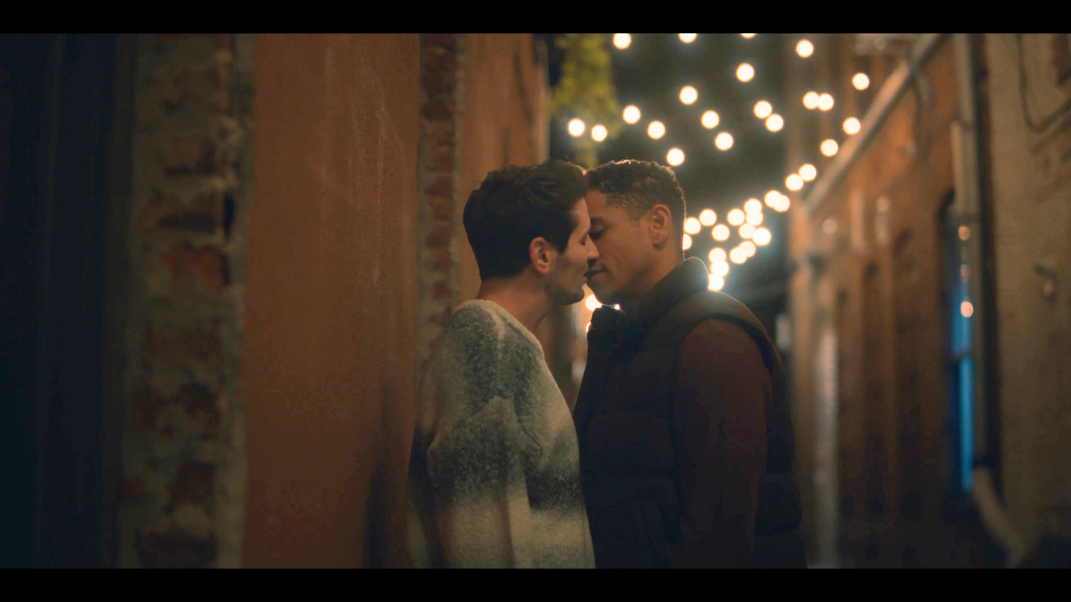 Nate and Daniel kissing beneath warm string lights